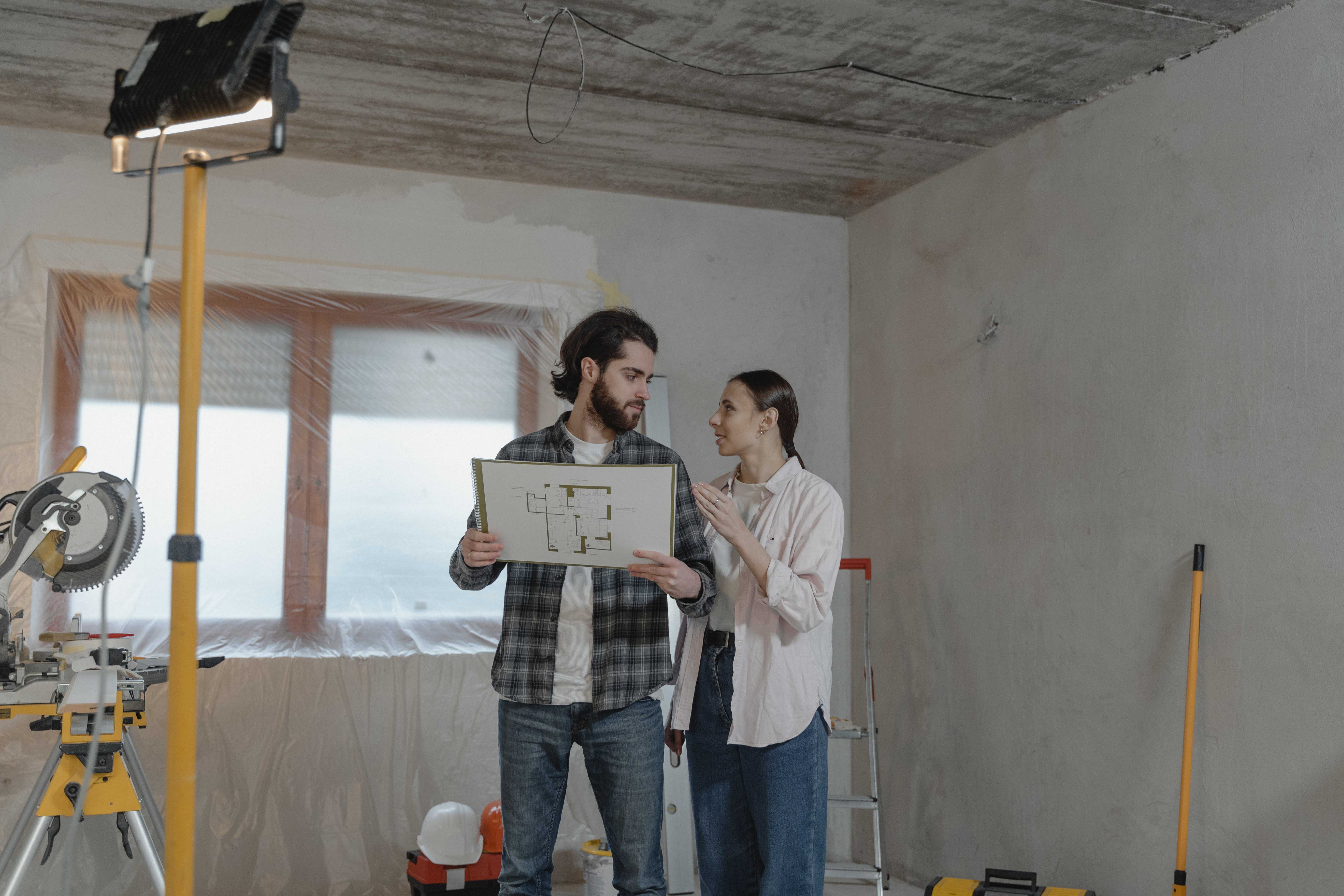 a man and a woman standing in a room with blueprints in hand